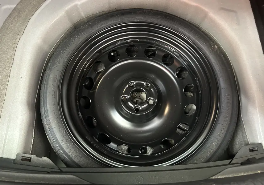 Gros plan sur la roue de secours noire en acier du coffre d'un Volkswagen Taigo blanc Pur TSI 110 DSG7 Style 2022.