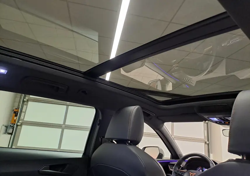 Vue intérieure du toit ouvrant panoramique du CUPRA LEON ST 2025, avec sièges noirs et éclairage d'ambiance violet.