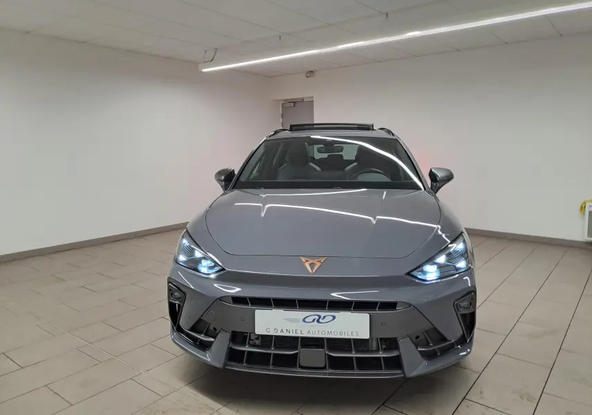 Vue avant d'une CUPRA Leon ST gris Graphène avec toit ouvrant panoramique et feux LED allumés dans un showroom.