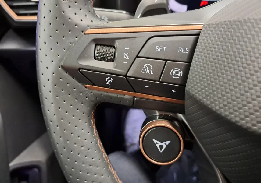 Gros plan sur la partie gauche du volant perforé avec surpiqûres cuivrées du CUPRA Leon ST gris Graphène, boutons de commande intégrés.