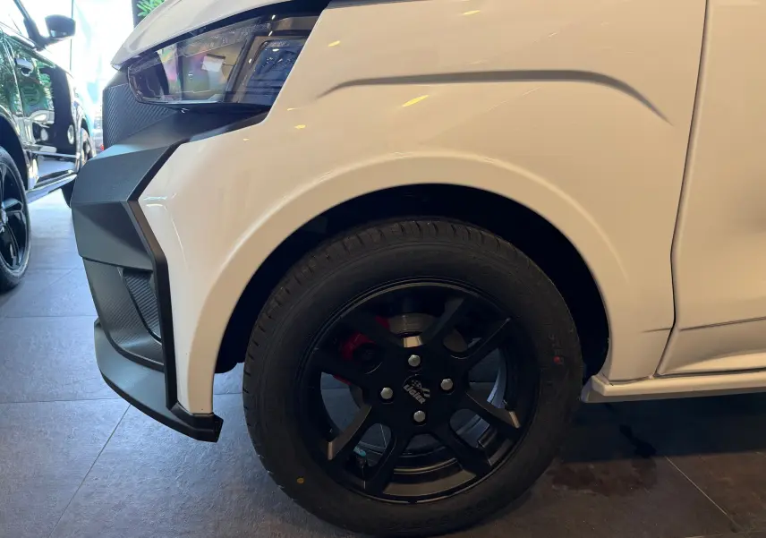 Gros plan sur la roue avant droite noire et l’aile blanche glacier d’une Ligier JS50 Select Revo D+ 2026 en intérieur showroom.