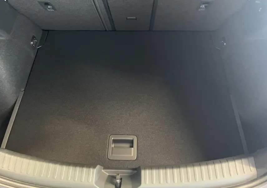 Coffre vide vu de dessus de la CUPRA Leon 1.5 eTSI Hybrid gris, avec tapis de sol noir et poignées intégrées.