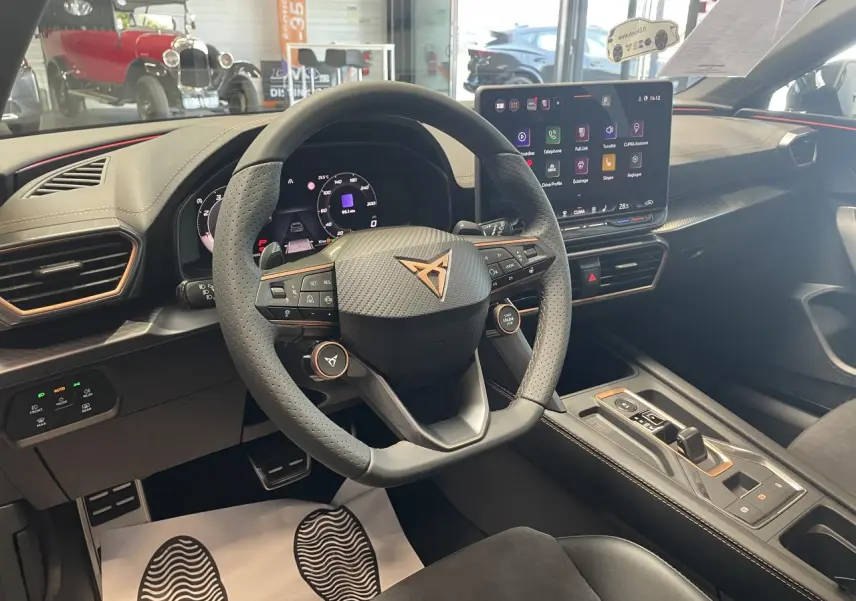 Vue intérieure du poste de conduite de la CUPRA Leon gris, volant perforé avec logo cuivré et écran tactile HD.