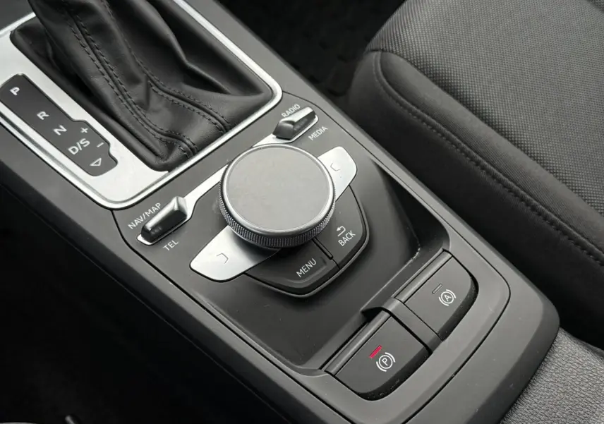 Gros plan sur la console centrale noire de l'Audi Q2 35 TFSI S-Line, montrant la molette MMI et le levier de vitesses automatique.
