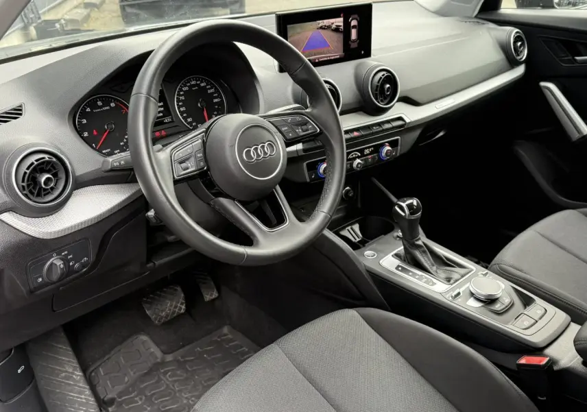 Intérieur noir de l'Audi Q2 35 TFSI 2023 vu côté conducteur, avec tableau de bord et écran caméra de recul.