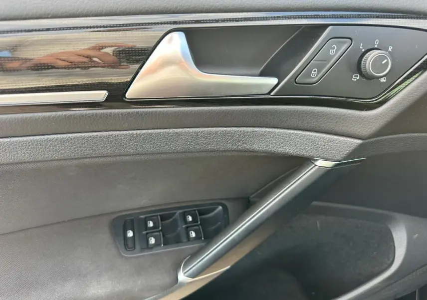 Vue rapprochée de la porte côté gauche de la Volkswagen Golf noire, avec commandes électriques et poignée argentée.