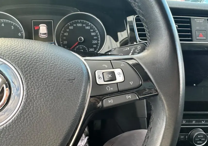 Gros plan sur le volant multifonctions noir de la Volkswagen Golf 2018, avec commandes intégrées et tableau de bord en arrière-plan.