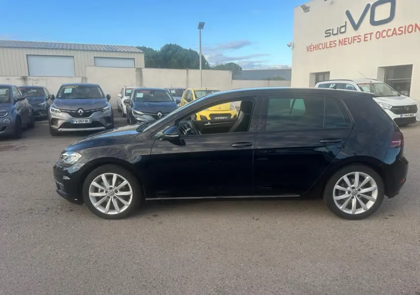 Profil côté gauche d'une Volkswagen Golf noire 2018 avec jantes alliage 17 pouces, stationnée en extérieur sur un parking.