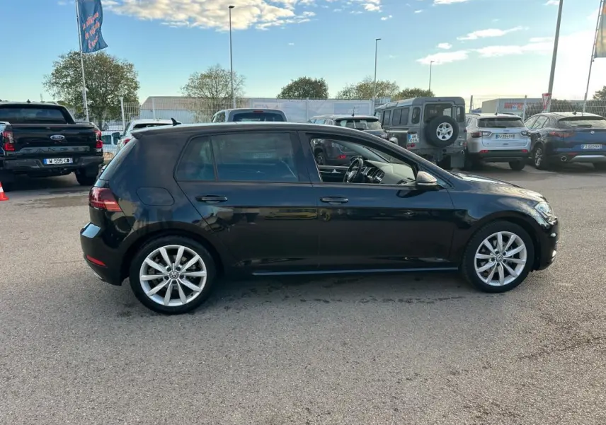 Profil côté gauche d'une Volkswagen Golf noire de 2018 avec jantes alliage 17 pouces sur parking extérieur.