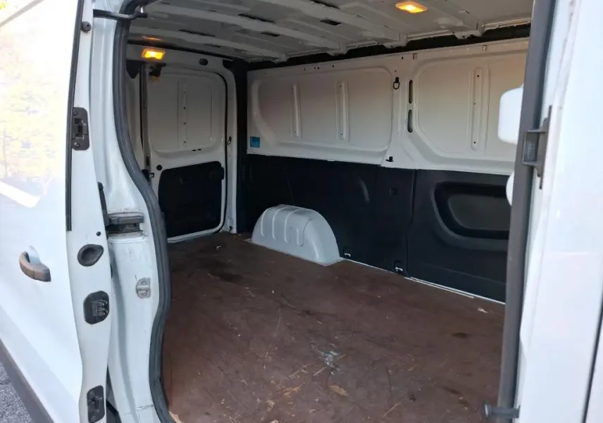 Vue intérieure du fourgon blanc Renault Trafic L2H1 2019, montrant l'espace de chargement avec plancher en bois et éclairage allumé.