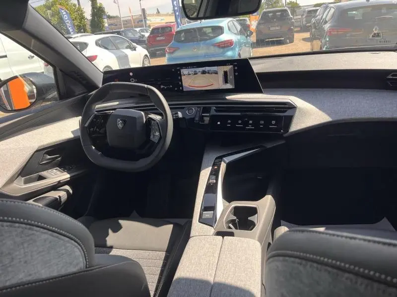 Vue intérieure avant du Peugeot 5008 Hybrid blanc Okénite, avec tableau de bord numérique et volant compact multifonction.