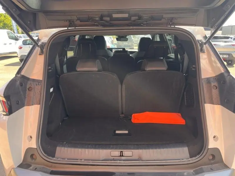 Vue arrière du coffre ouvert d’un Peugeot 5008 blanc Okénite avec sièges rang 3 relevés et un triangle de signalisation orange posé.