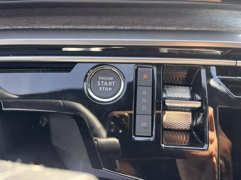 Gros plan sur la console centrale noire brillante du Peugeot 5008 Hybrid avec bouton start/stop et commandes de boîte automatique.