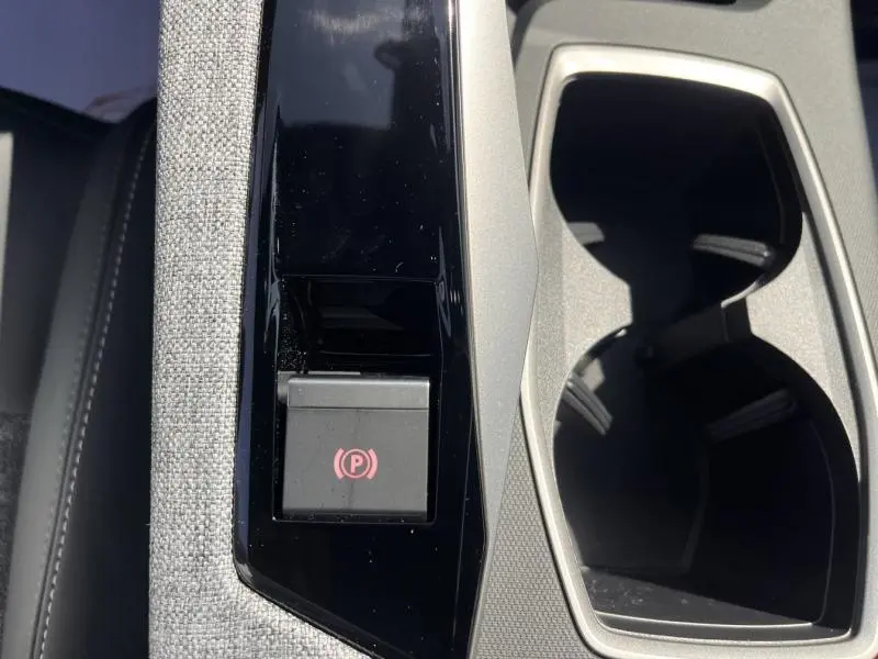 Gros plan sur la console centrale du Peugeot 5008 Hybrid blanc, montrant le bouton de frein à main électronique et les porte-gobelets.