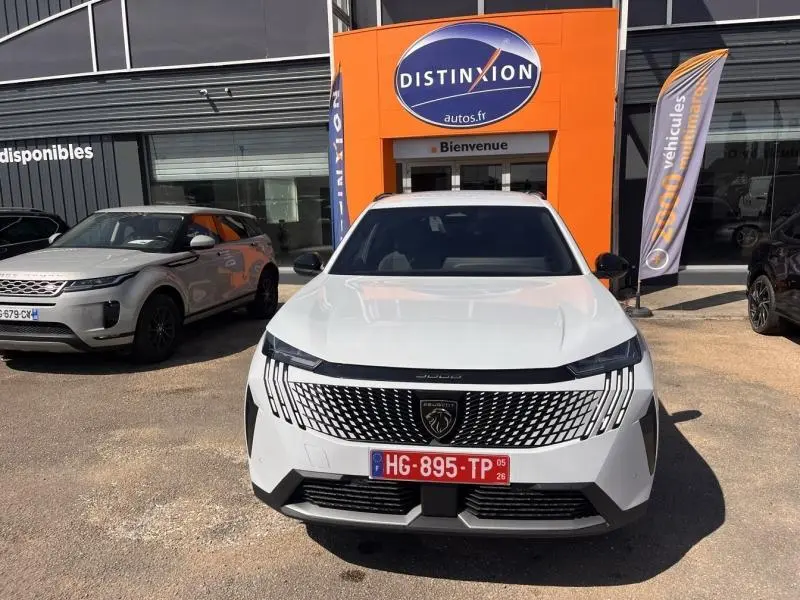 Vue de face du Peugeot 5008 Hybrid blanc Okénite avec calandre distinctive et plaque rouge temporaire.