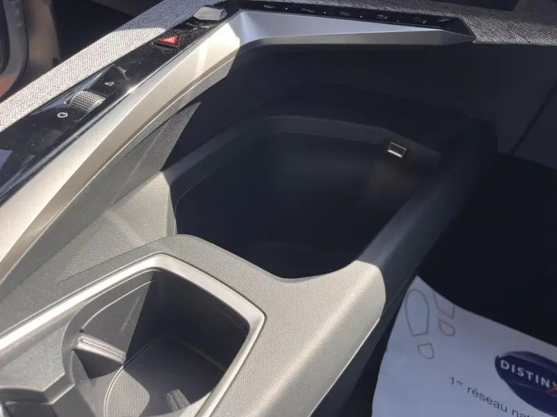 Gros plan sur la console centrale noire du Peugeot 5008 Hybrid 2025, avec porte-gobelets et prise USB intégrée.