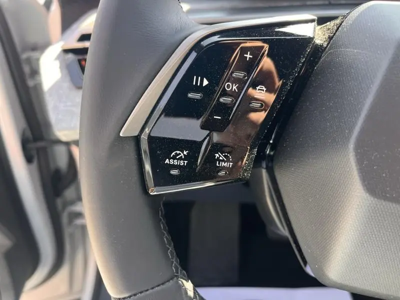 Gros plan sur les commandes multifonctions noires à gauche du volant cuir du Peugeot 5008 Hybrid blanc Okénite.