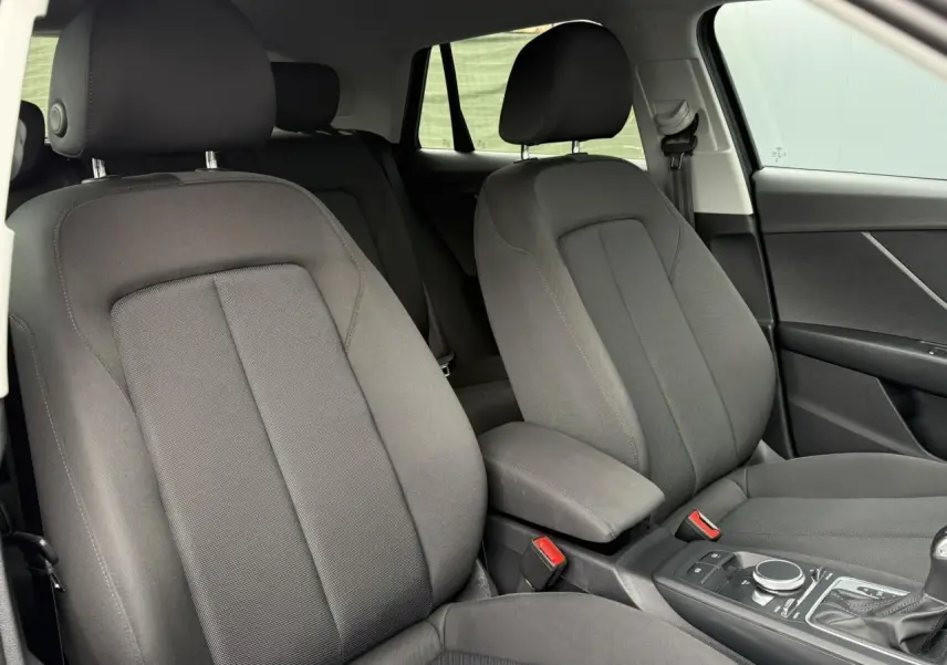 Intérieur de l'Audi Q2 35 TFSI 2023, vue des sièges avant gris foncé et console centrale avec commandes automatiques.