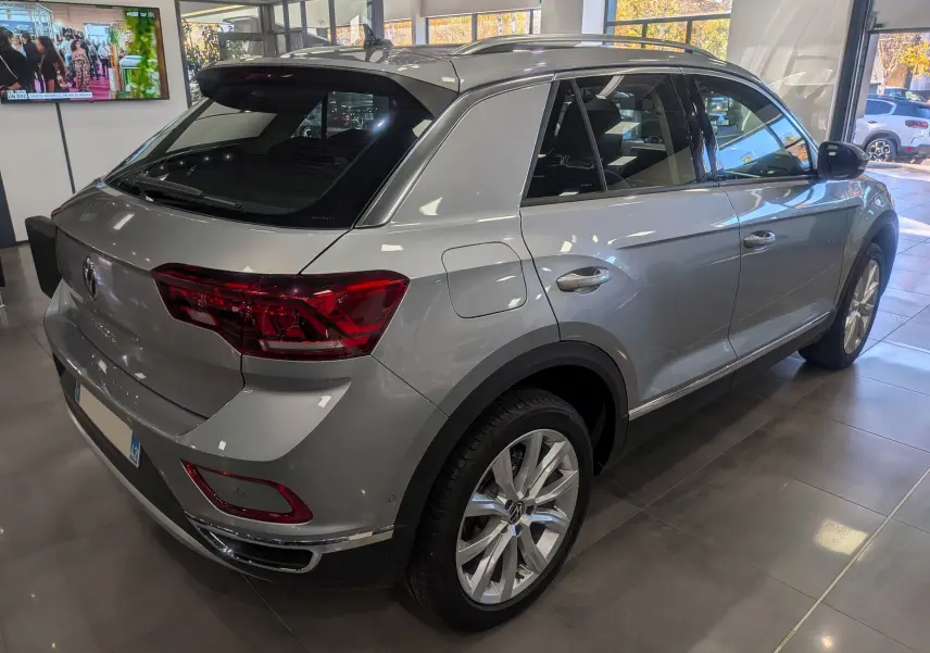 Volkswagen T-Roc gris pyrite vu en 3/4 arrière droit, avec jantes alliage et feux arrière LED en showroom.