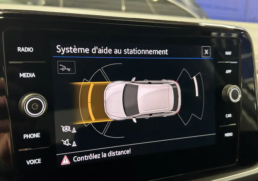 Écran du système d'aide au stationnement montrant un Volkswagen T-Roc gris Indium vu de dessus avec alertes de proximité avant.