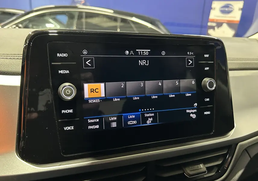 Écran tactile central du Volkswagen T-Roc 2025 affichant la radio NRJ, avec tableau de bord noir en arrière-plan.