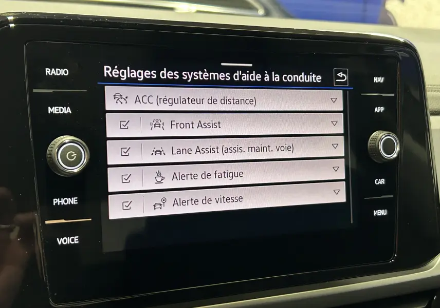 Écran tactile intérieur du Volkswagen T-Roc affichant les réglages des aides à la conduite, avec commandes autour en noir brillant.