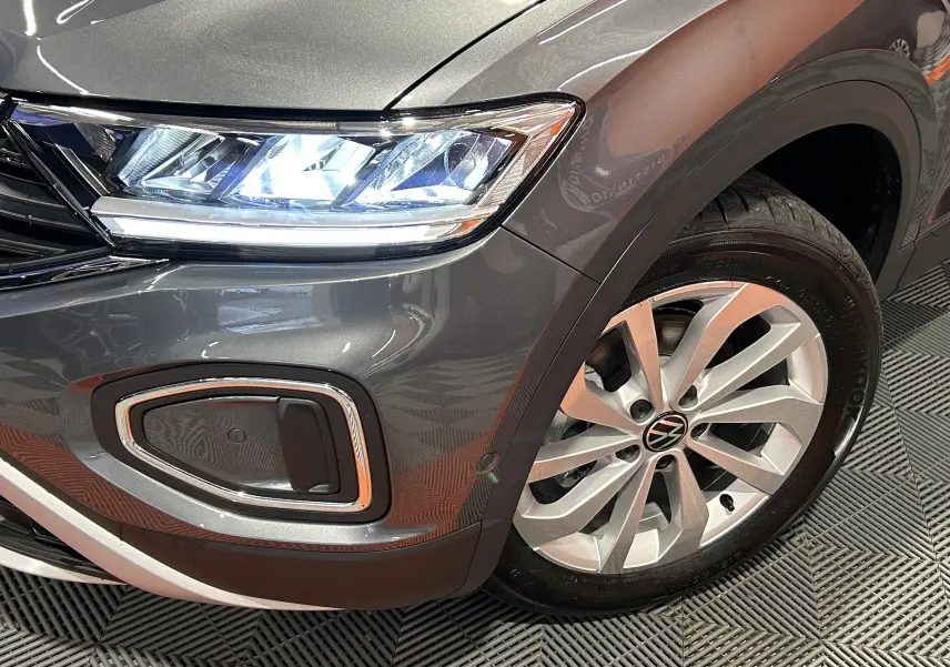 Gros plan sur l'avant droit du Volkswagen T-Roc gris Indium Metal, avec phare LED allumé et jante alliage visible.