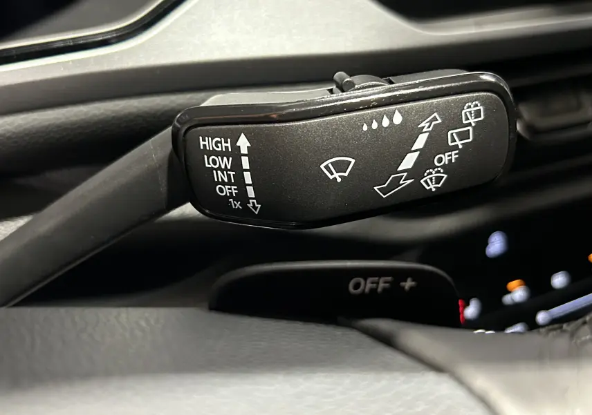 Gros plan sur la manette d’essuie-glace noire à gauche du volant dans l’habitacle du Volkswagen T-Roc gris Indium.
