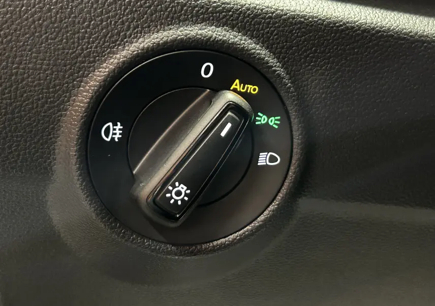 Gros plan sur le sélecteur de phares du Volkswagen T-Roc 2025, avec mode automatique activé, sur tableau de bord noir.