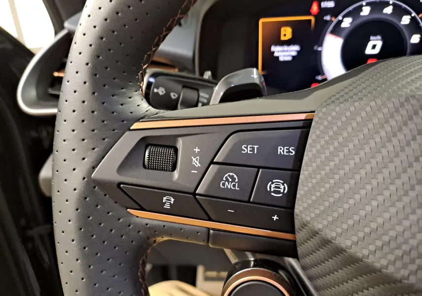 Gros plan sur les commandes du volant perforé avec insert cuivre du CUPRA TERRAMAR 1.5 eTSI 150 DSG7, tableau de bord en arrière-plan.