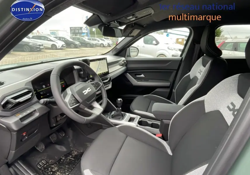 Vue intérieure côté conducteur du Dacia Duster 2026 vert kaki, avec tableau de bord numérique et sièges bi-ton gris et noir.