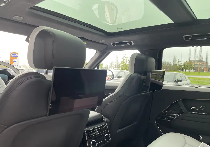Vue intérieure arrière du Range Rover Sport P440 HSE R-Dynamic 2023, avec écrans TV intégrés aux appuie-têtes et ciel de pavillon en suédine noire.