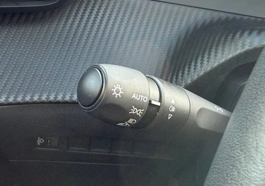 Gros plan sur la commande des phares automatiques dans l’habitacle du Peugeot e-2008 bleu Obsession.