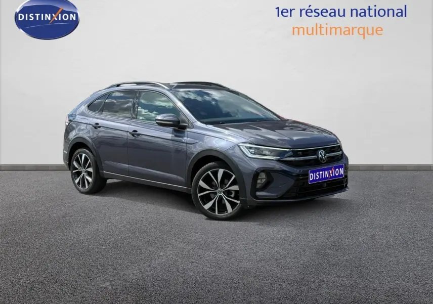 Volkswagen Taigo gris Ascot en vue 3/4 avant droit, avec jantes alliage et barres de toit visibles.