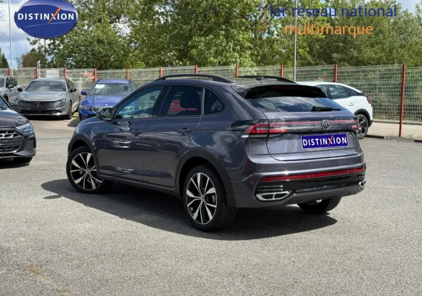 Volkswagen Taigo gris Ascot vu en 3/4 arrière droit avec jantes alu et barres de toit sur parking.