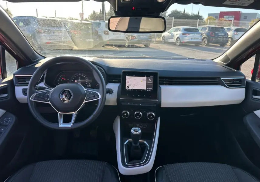 Vue intérieure avant de la Renault Clio rouge foncé 2021, volant cuir, écran tactile et levier de vitesse manuel visibles.