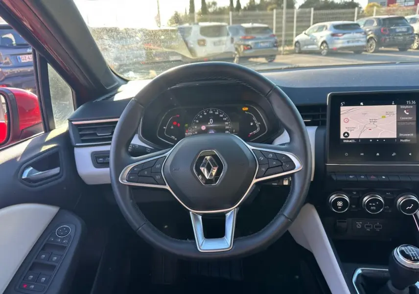 Vue intérieure centrée sur le volant cuir et tableau de bord d'une Renault Clio rouge foncé, avec écran tactile et boîte manuelle.