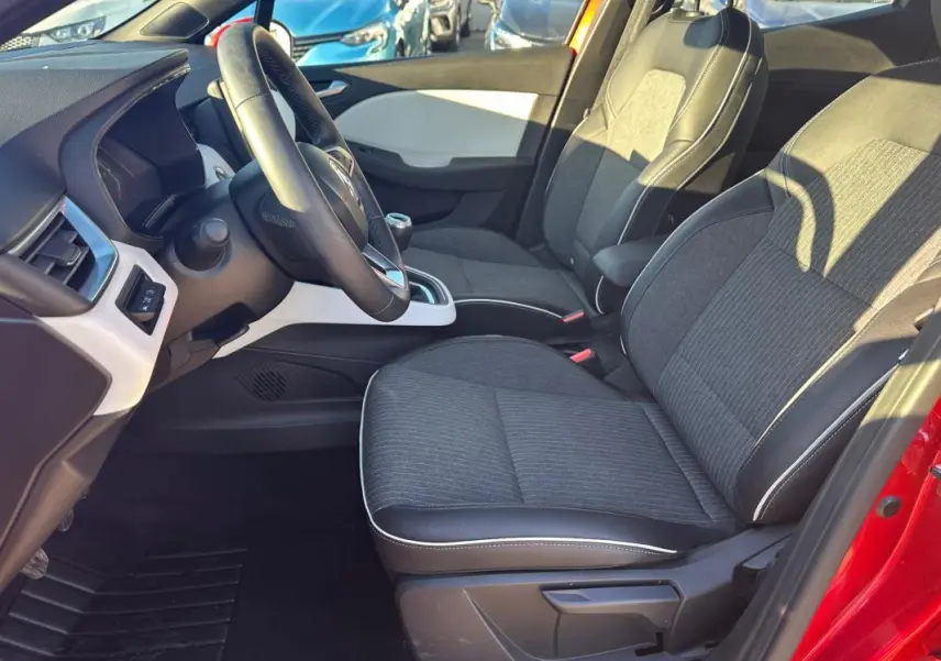 Vue intérieure côté conducteur de la Renault Clio rouge foncé, sièges tissu noir avec surpiqûres blanches et volant cuir.