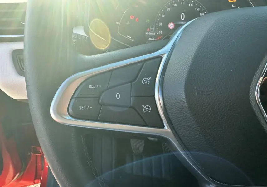 Gros plan sur le volant cuir de la Renault Clio rouge foncé, montrant les commandes du régulateur de vitesse côté gauche.