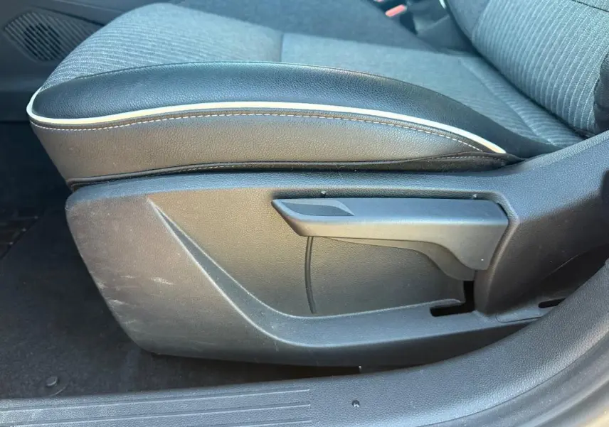 Gros plan sur l'accoudoir central en cuir noir avec surpiqûres blanches, siège tissu gris de la Renault Clio rouge foncé.