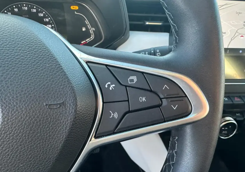 Gros plan sur le volant cuir de la Renault Clio rouge foncé 2021, avec commandes multifonctions et tableau de bord partiellement visible.