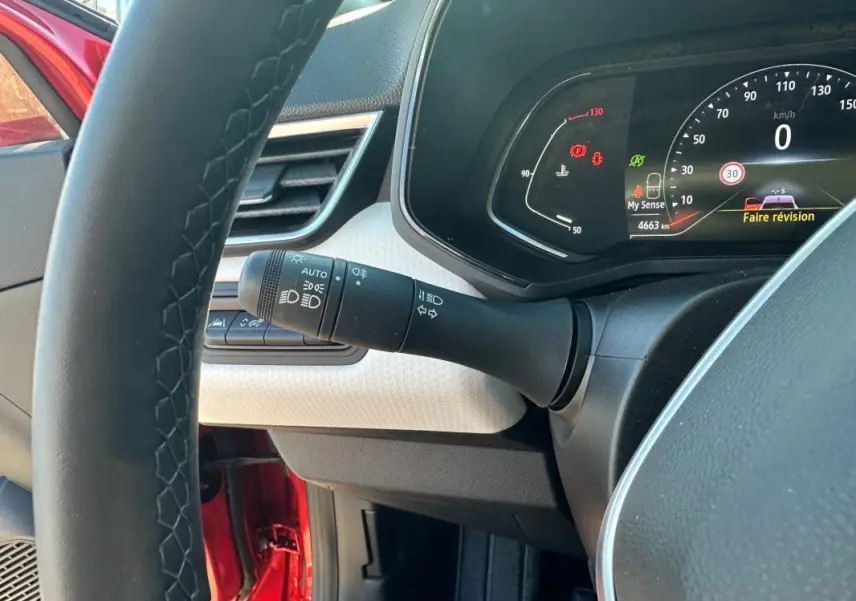 Vue intérieure côté conducteur de la Renault Clio rouge foncé 2021, tableau de bord et volant cuir visibles.