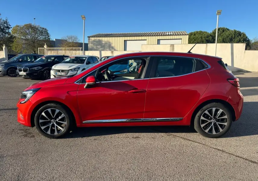 Profil côté gauche d'une Renault Clio rouge foncé de 2021 avec jantes alliage 17 pouces sur un parking extérieur.