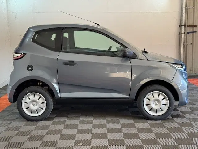 Vue de profil côté gauche d'une Aixam Ambition 0.5 City Pack gris foncé avec rétroviseur caméra conducteur.