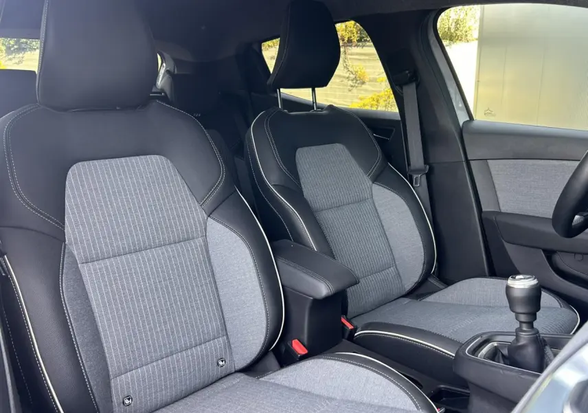 Vue intérieure rapprochée des sièges avant gris et noirs avec accoudoir central et levier de vitesse manuel d’une Renault Clio 2025.