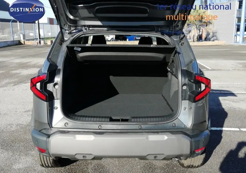 Vue arrière du Dacia Duster gris schiste métal 2026 avec coffre ouvert sur parking extérieur.