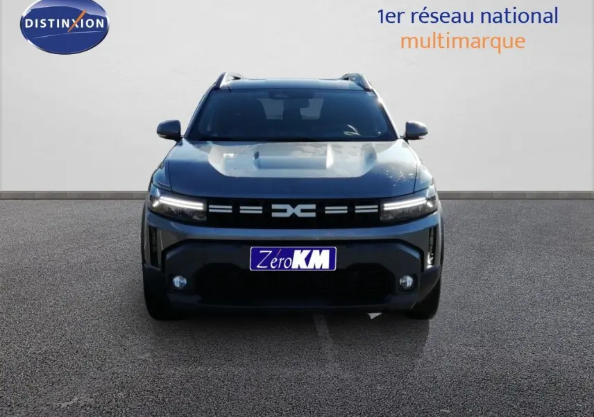 Vue frontale du Dacia Duster TCE MHEV 140ch Journey gris schiste métal avec calandre distinctive et feux LED allumés.