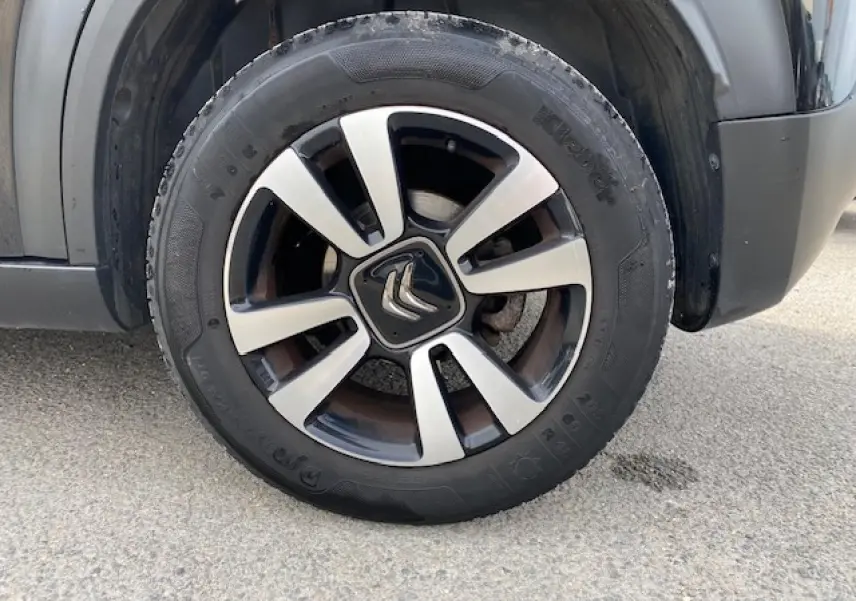 Gros plan sur la roue galette noire et argentée du côté gauche d’un Citroën C3 Aircross noir de 2019.