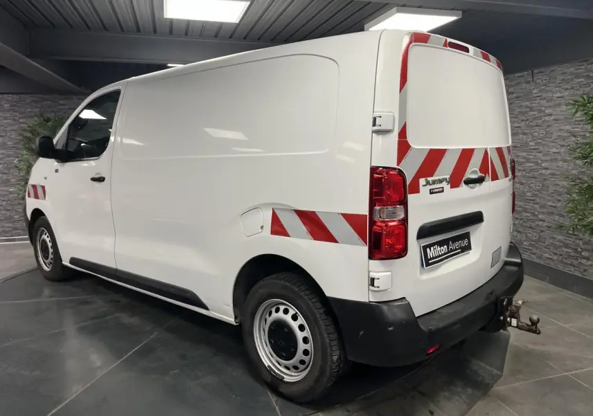 Vue 3/4 arrière droite d'un utilitaire blanc Citroën Jumpy 2019 avec bandes réfléchissantes rouges et attelage crochet.