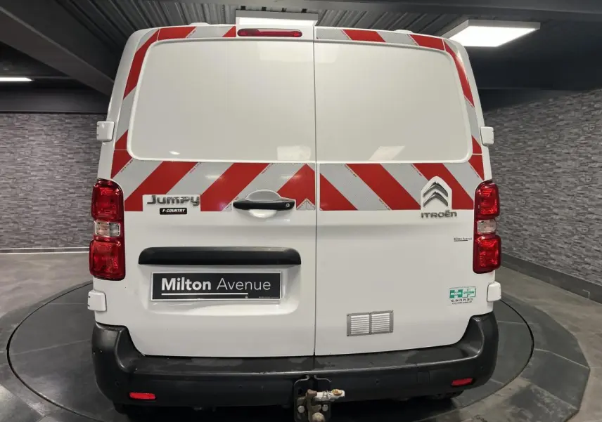 Vue arrière d'un Citroën Jumpy blanc avec bandes rouges diagonales et attelage crochet mixte visible.